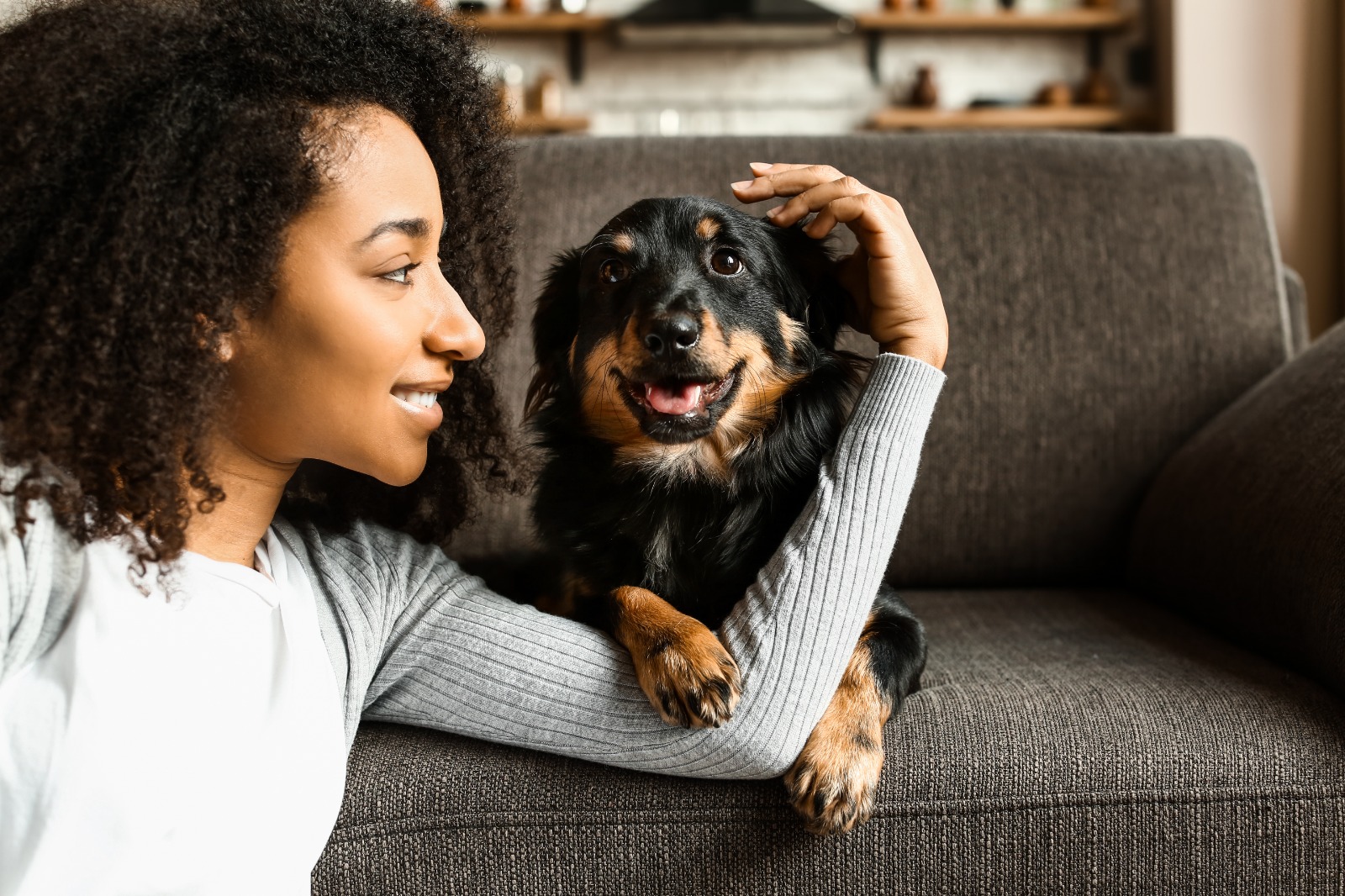 A woman sitting with her long-haired dachshund on a sofa at home