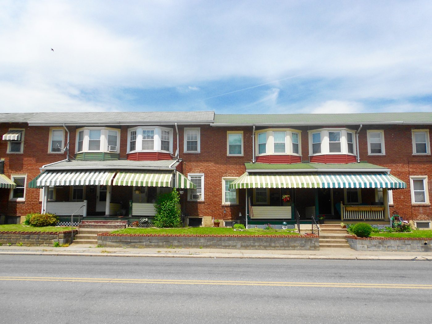A terrace of brick rowhouses with awnings along a residential street