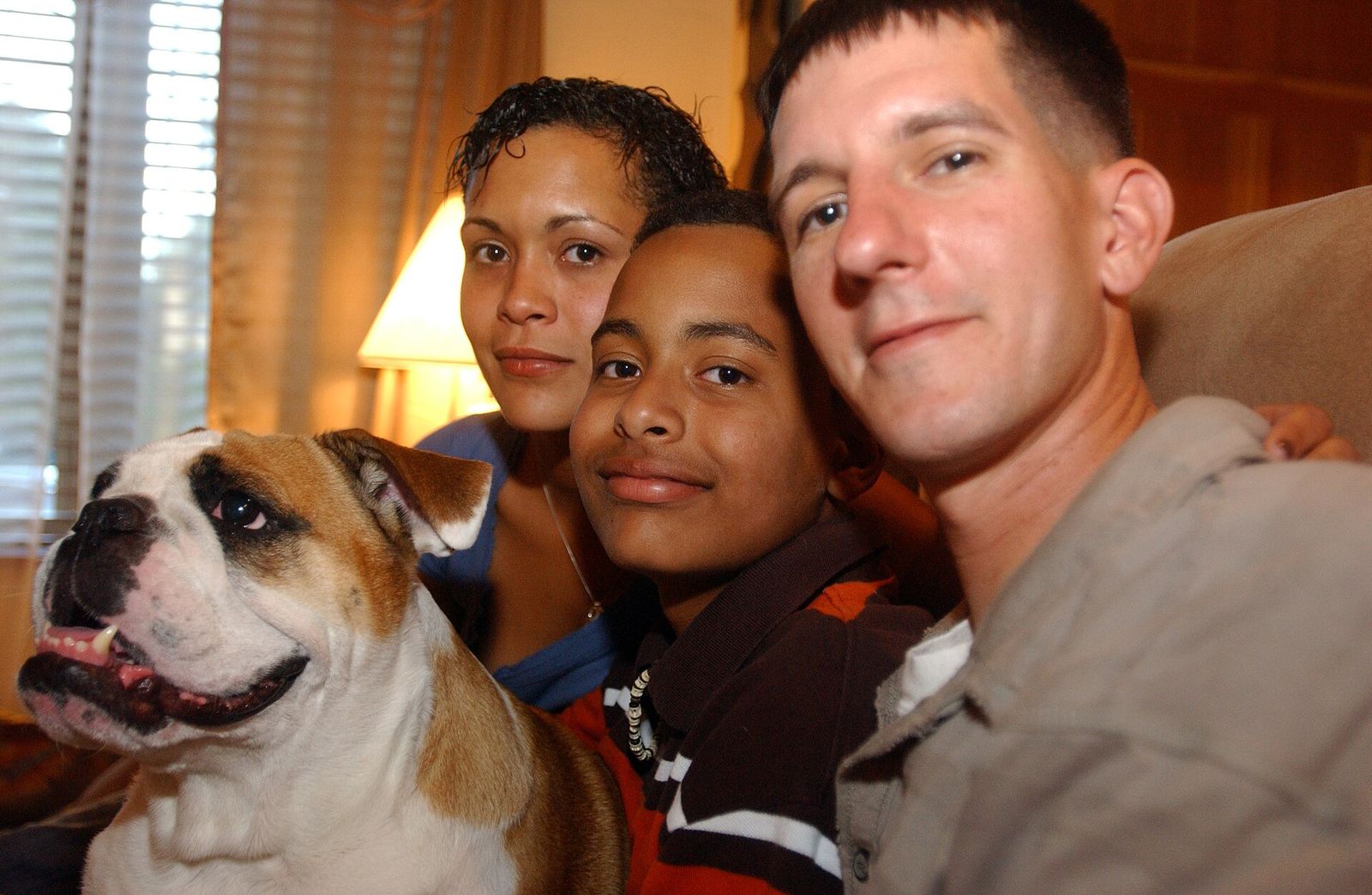 Soldier, spouse and son smiling on a couch beside their English bulldog