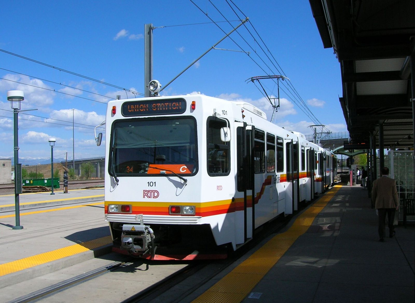 White RTD light rail train with orange stripes stopped at a Denver platform