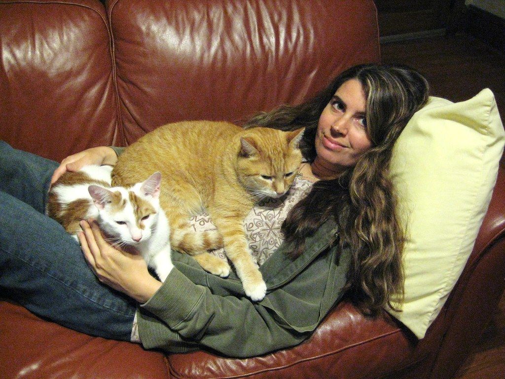 Woman relaxing on a leather couch with two cats resting on her lap