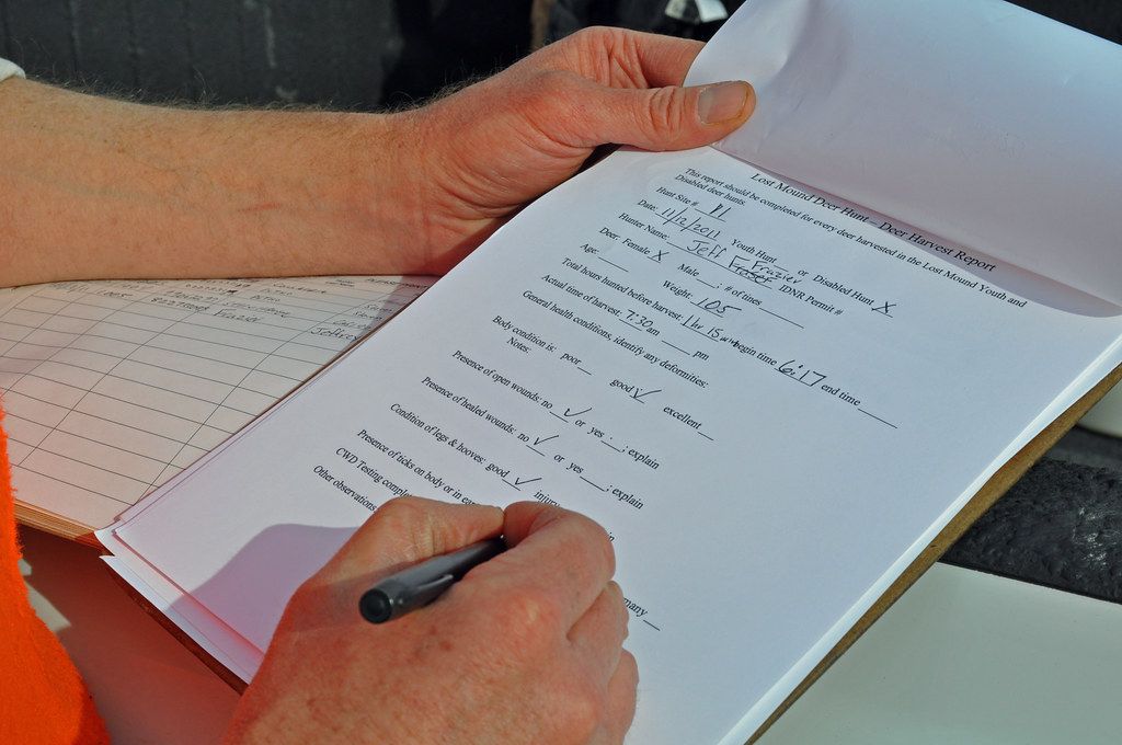 Hand holding a pen while filling in a printed data sheet on a clipboard