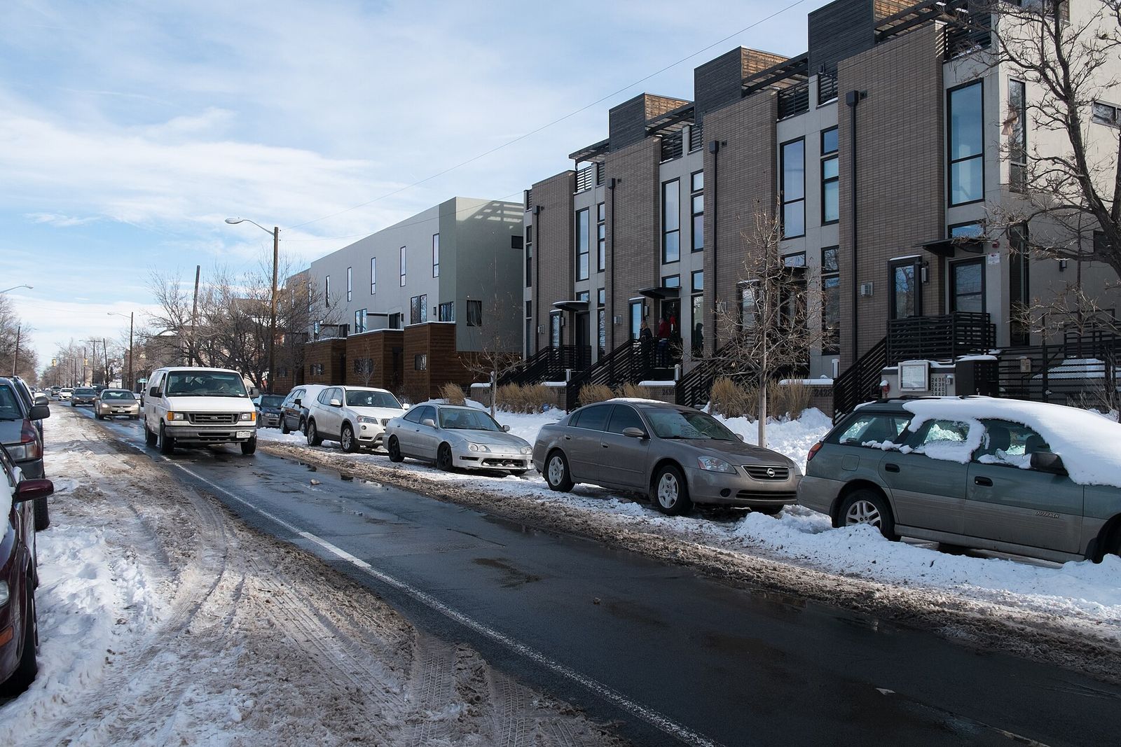 Row of modern townhouses along a snowy street with parked cars