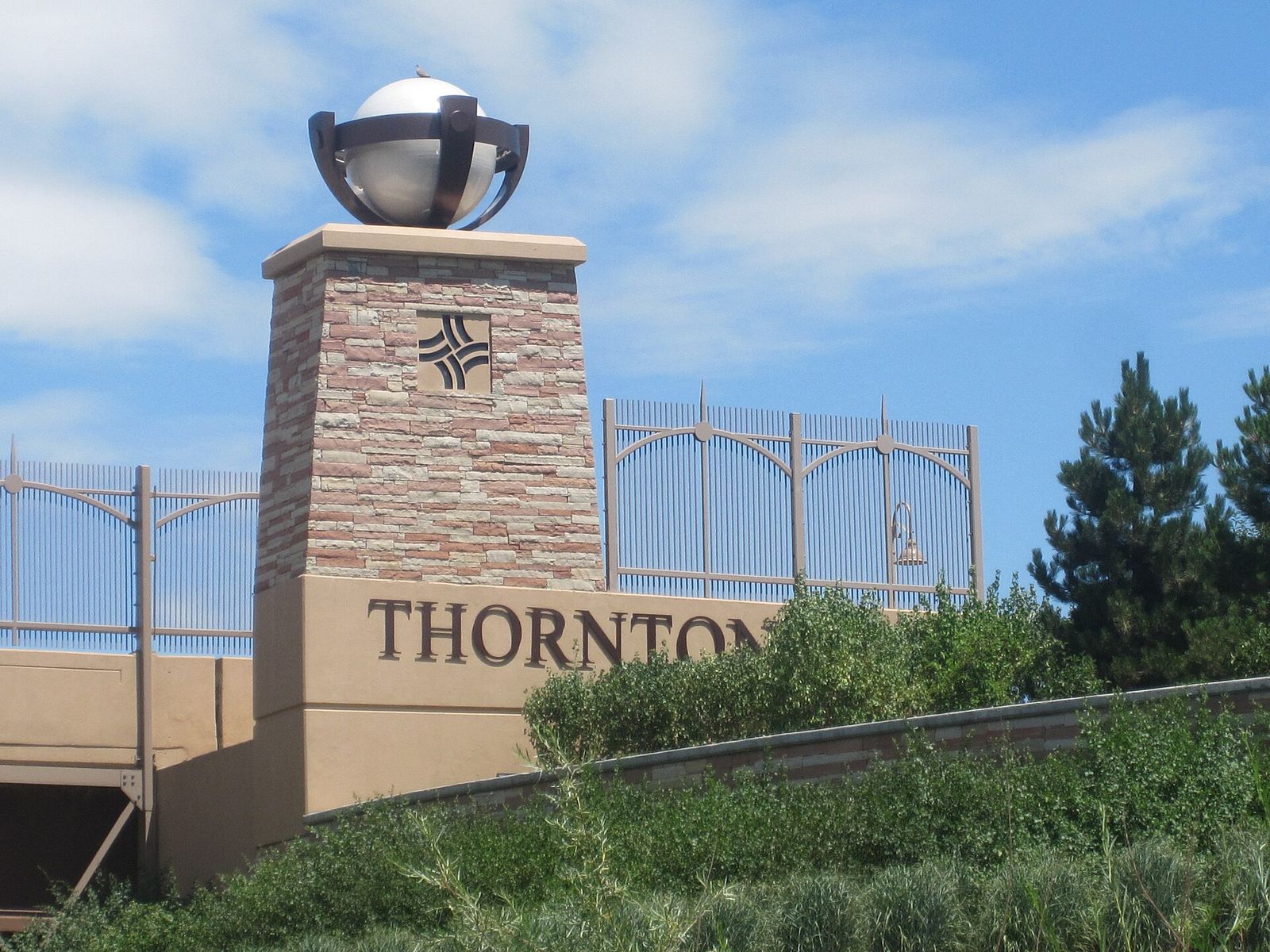 Stone Thornton city entry monument topped with a metal globe beside landscaping