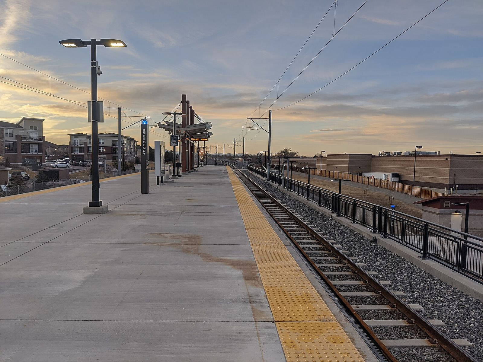 Empty commuter rail platform with light poles at Thornton Crossroads 104th station at sunset