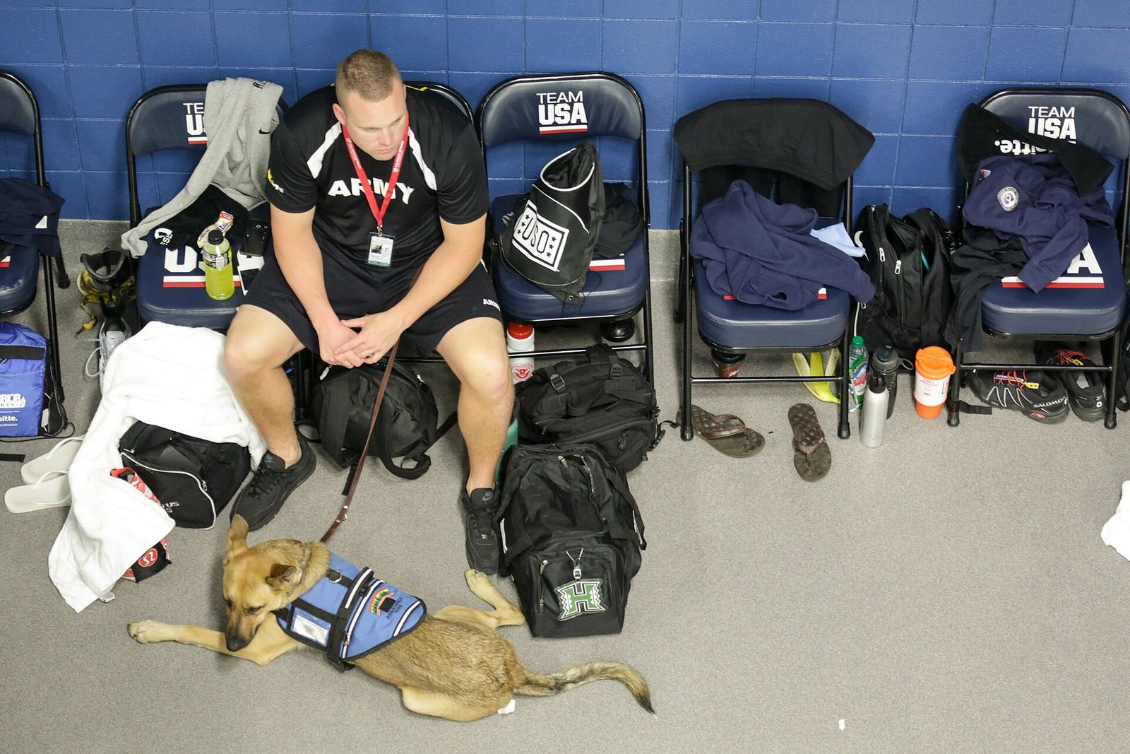 Army veteran athlete seated in a locker area at the 2014 Warrior Games with his service dog resting at his feet