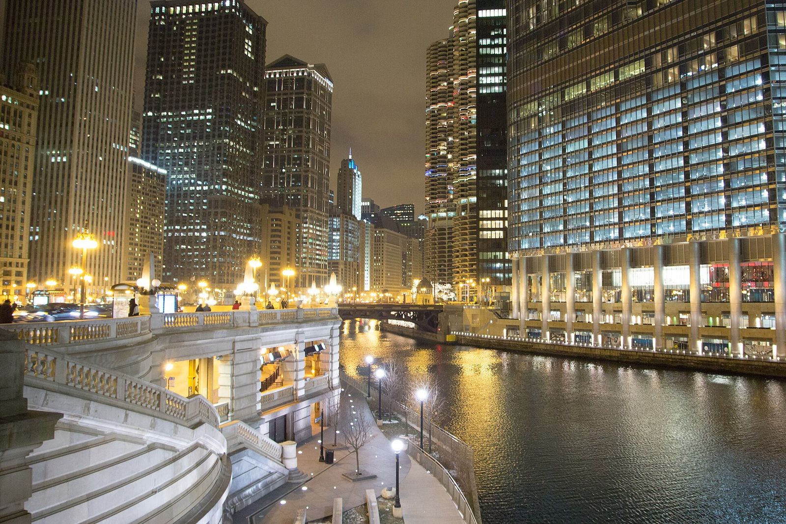 Chicago Riverwalk and river lit at night between downtown towers