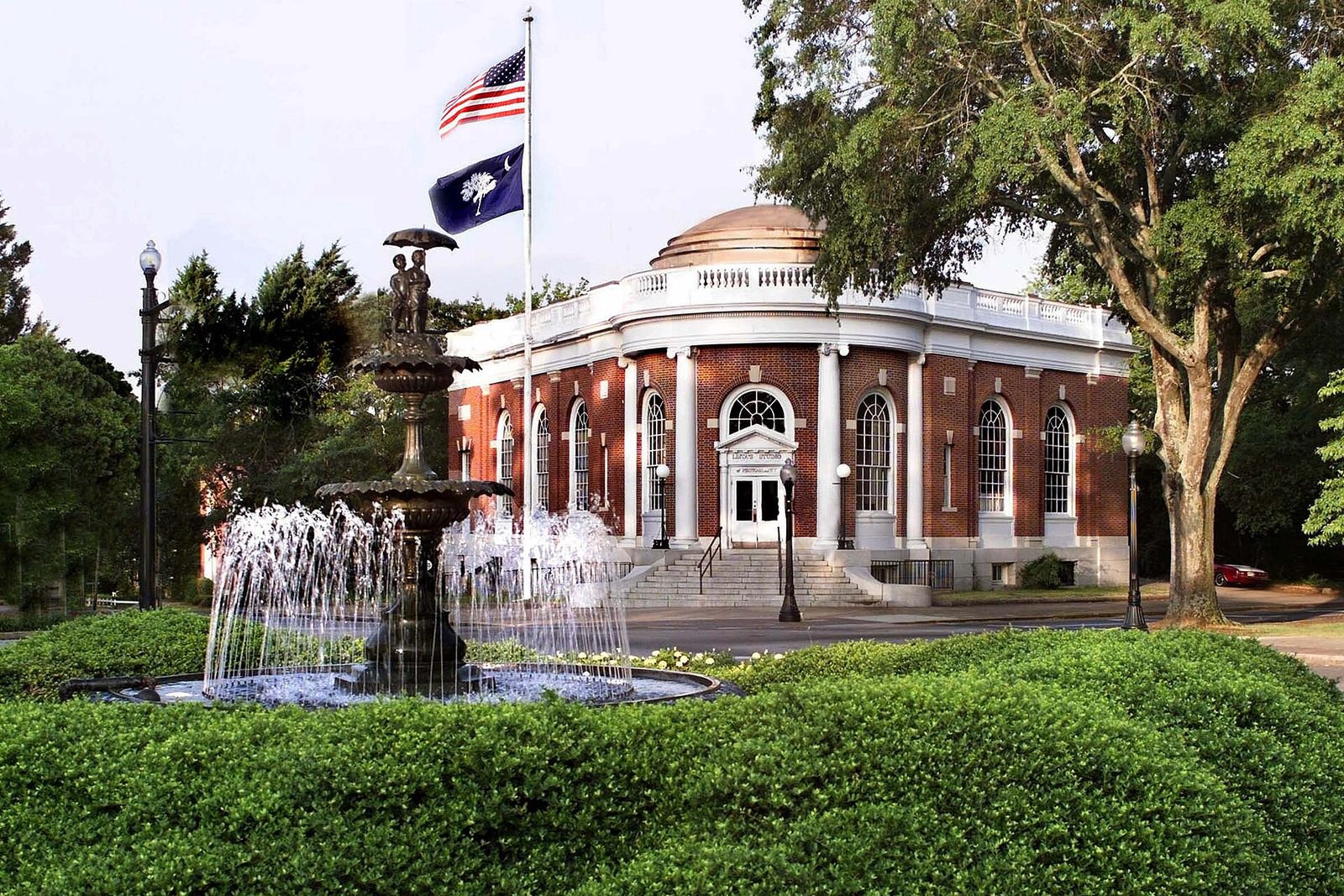 Historic brick post office in Aiken with a fountain and flags in front