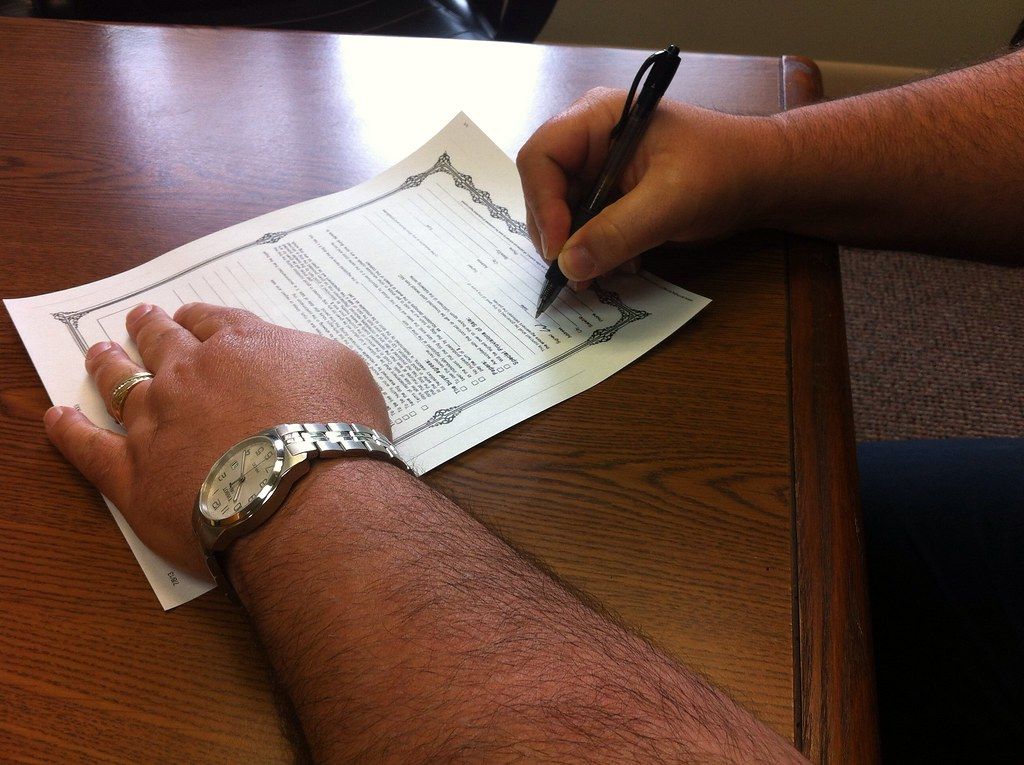 Hand wearing a wristwatch signing a printed form at a wooden desk