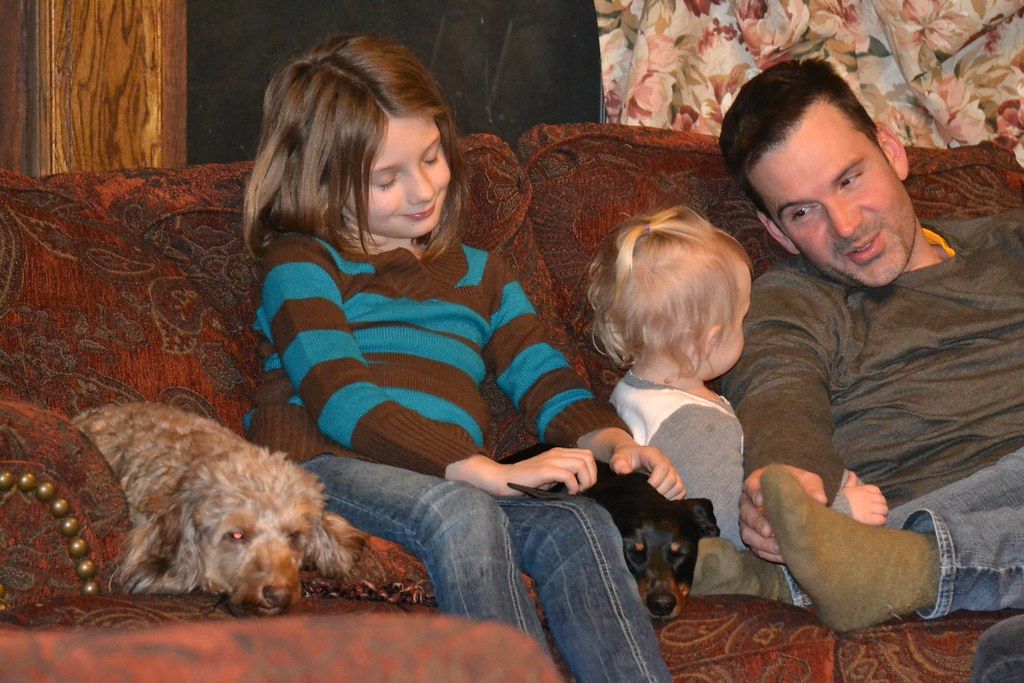 Family sitting on a patterned couch with a small shaggy dog curled beside them