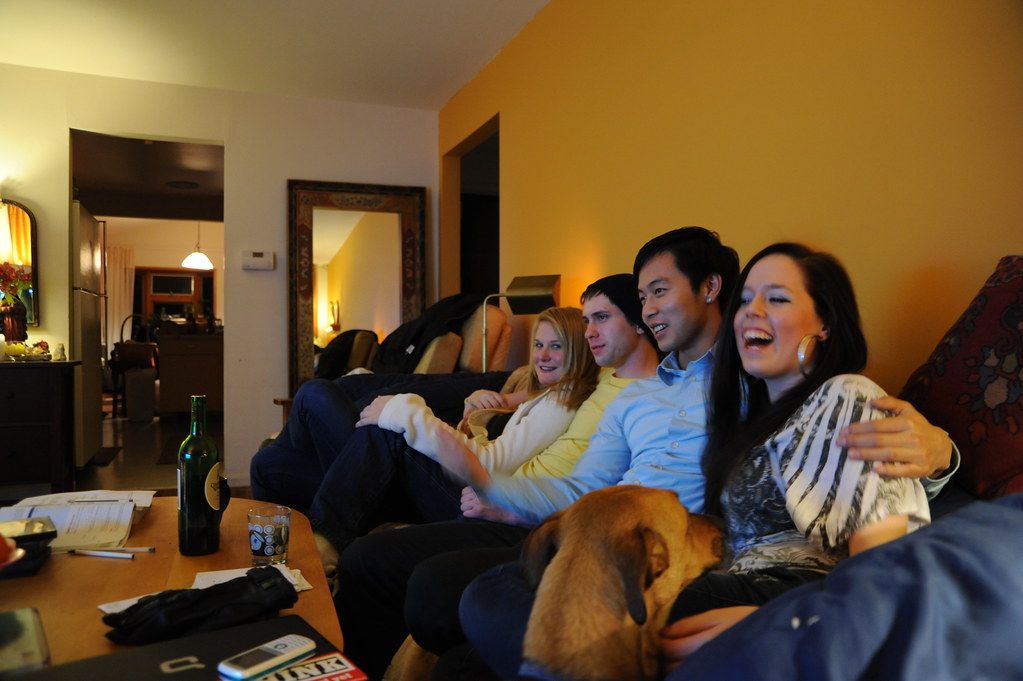 Friends laughing on a sofa in a living room with a dog lying at their feet