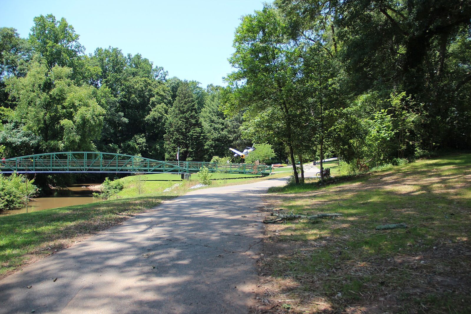 Paved Swamp Rabbit Trail winding through green trees near a small bridge in Greenville