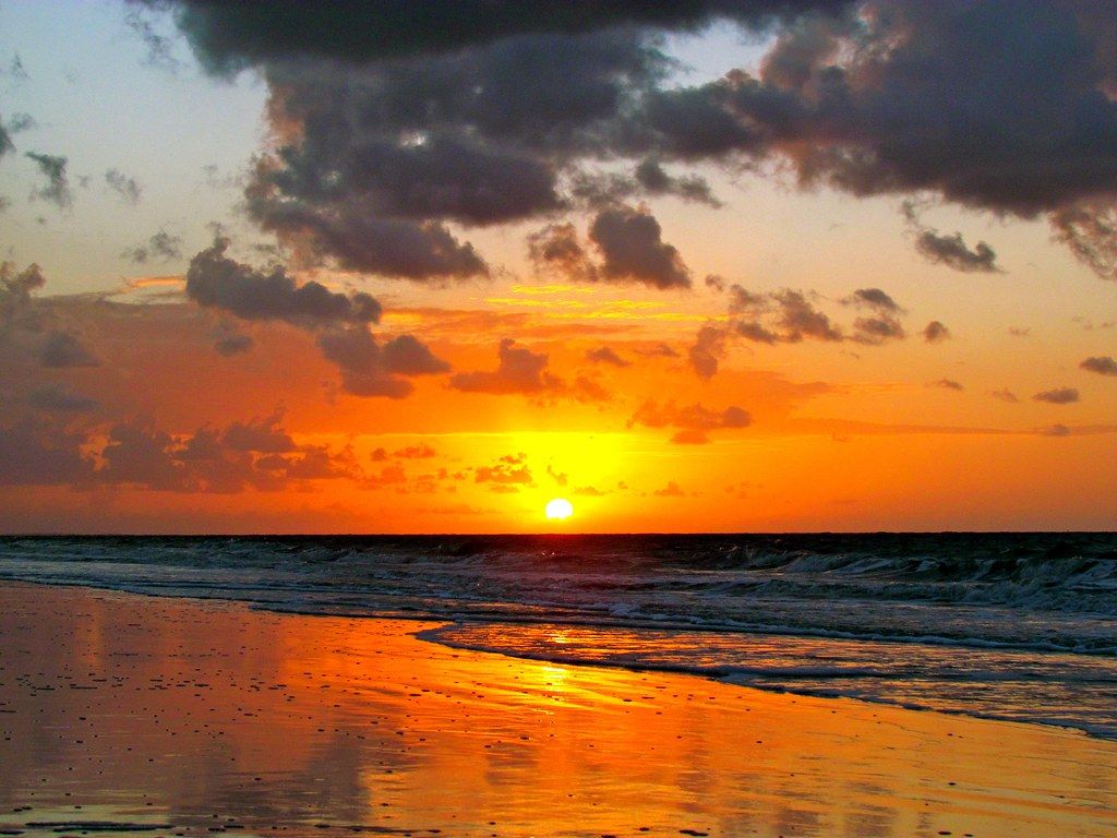 Orange sunset reflected on wet sand along a Hilton Head Island beach