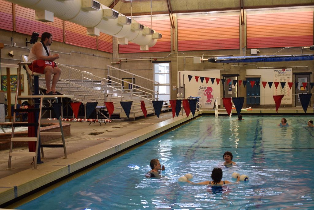 Indoor community pool with swimmers and lane lines under colorful flags