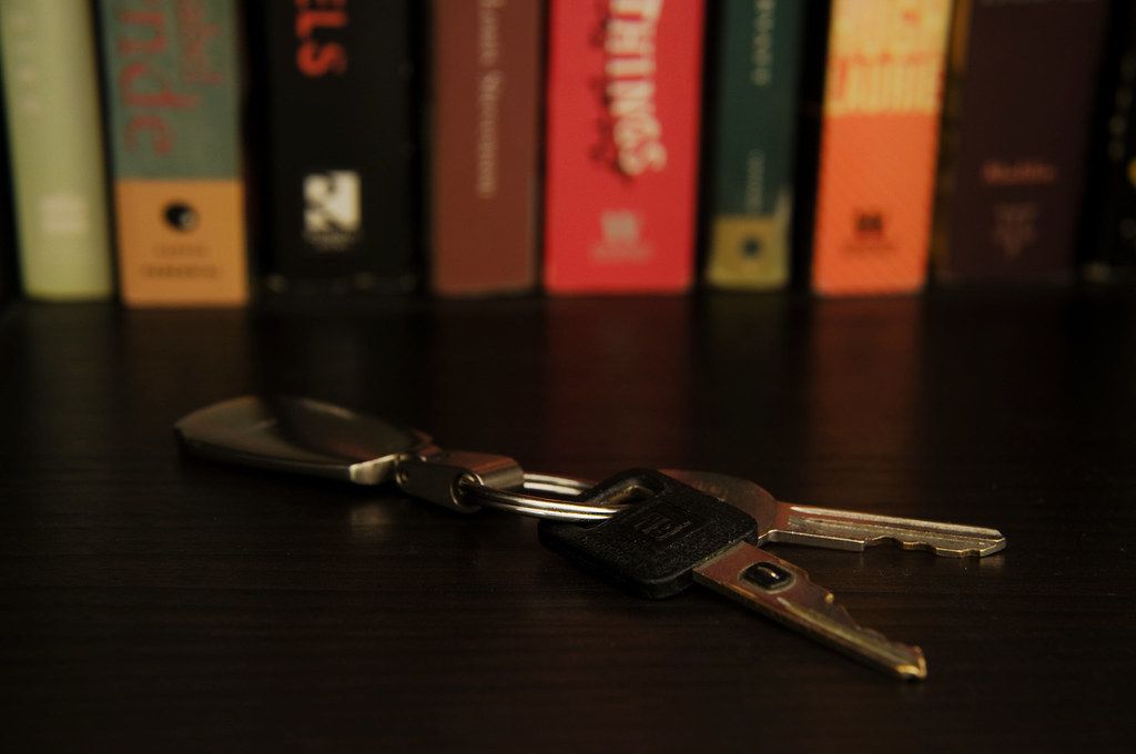 A set of house keys lying on a dark table in front of a row of books
