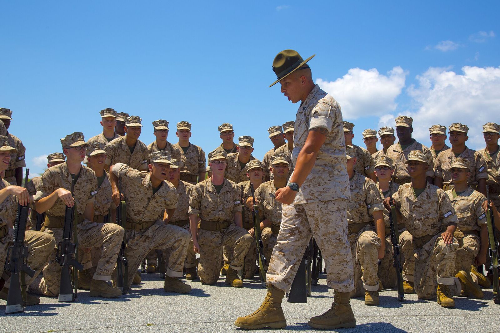 Drill instructor walking past rows of Marine recruits kneeling in formation at Parris Island
