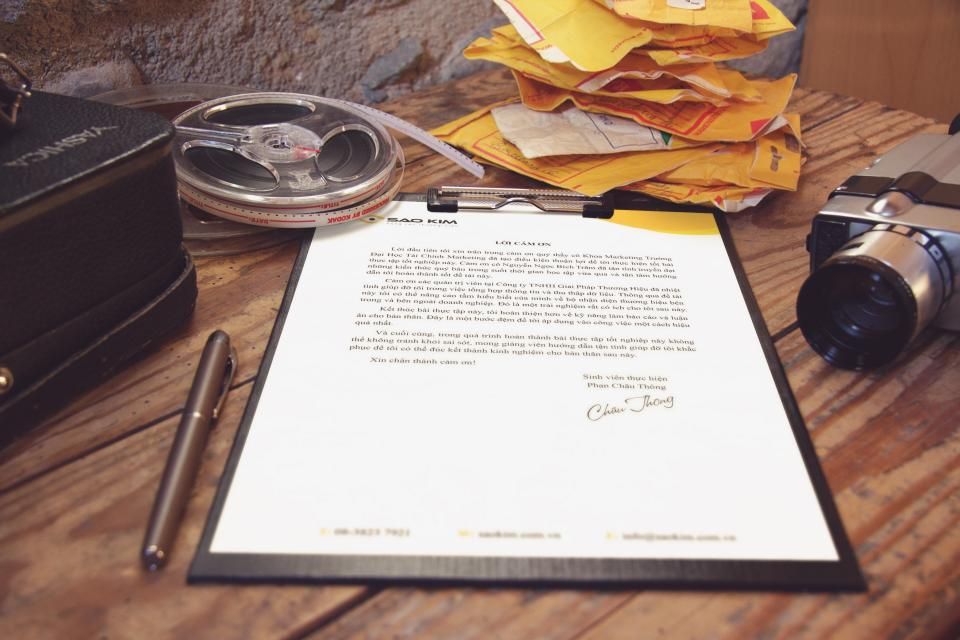 Signed typed letter on a clipboard beside a pen, film reel and camera on a wooden desk
