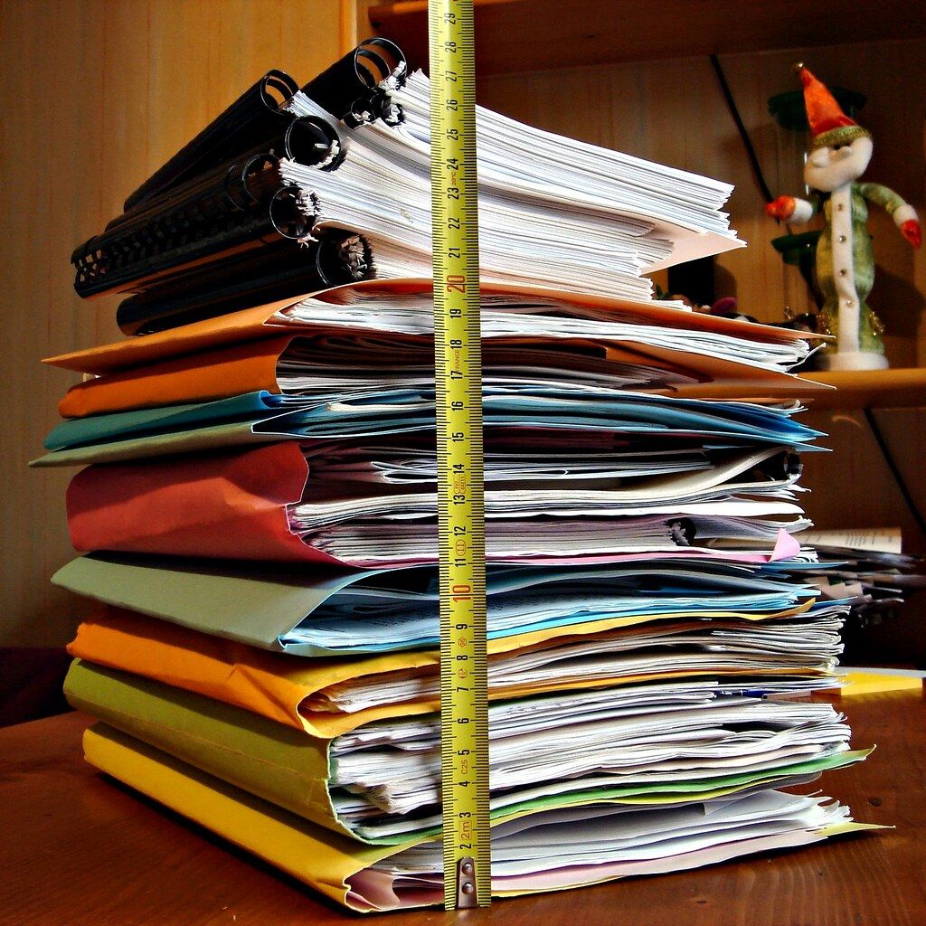 Tall stack of colorful file folders and binders measured against a yellow tape measure