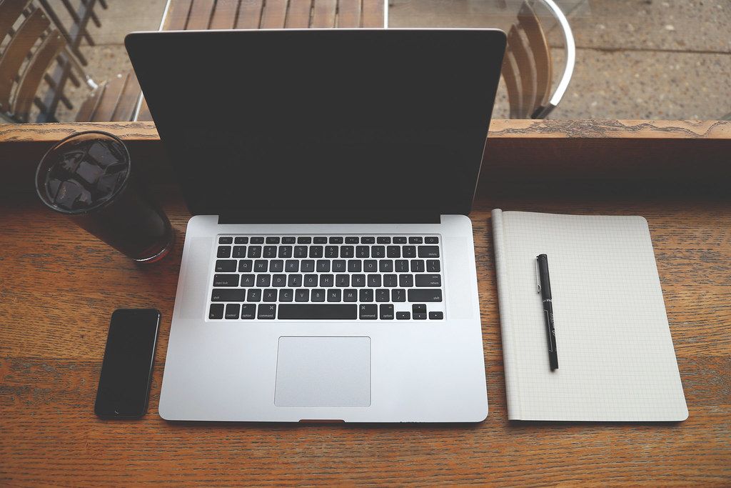 Laptop with a phone, closed notebook and pen on a wooden table