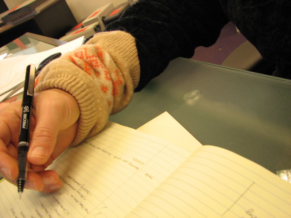 Hand in a knit glove writing with a pen in an open notebook