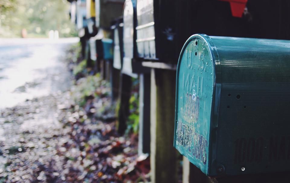 Row of teal and silver mailboxes along a leafy path