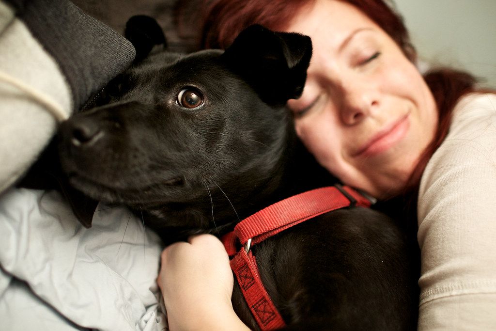 Smiling woman resting her head against a black dog wearing a red collar