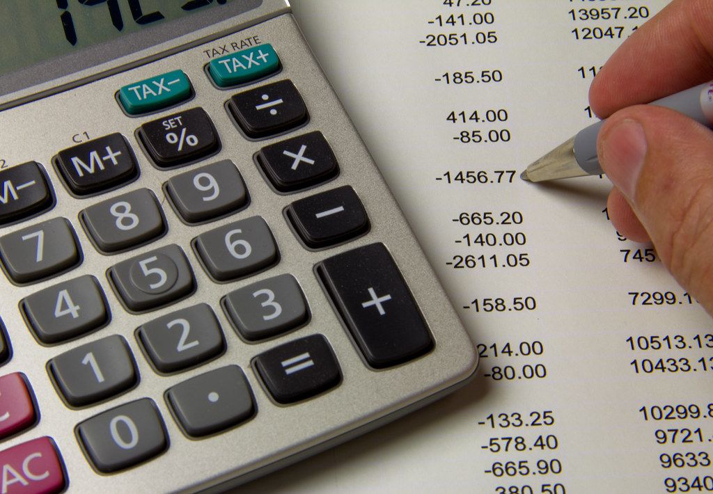 Pen pointing at columns of figures beside a desktop calculator