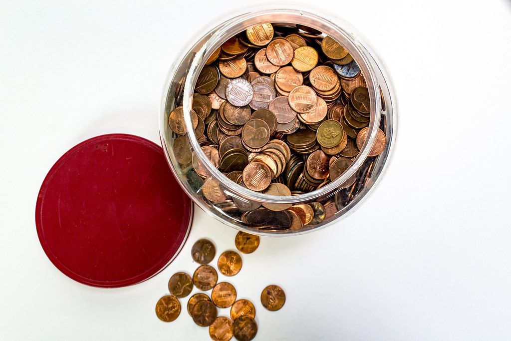 Glass jar full of pennies with coins spilling onto a white surface