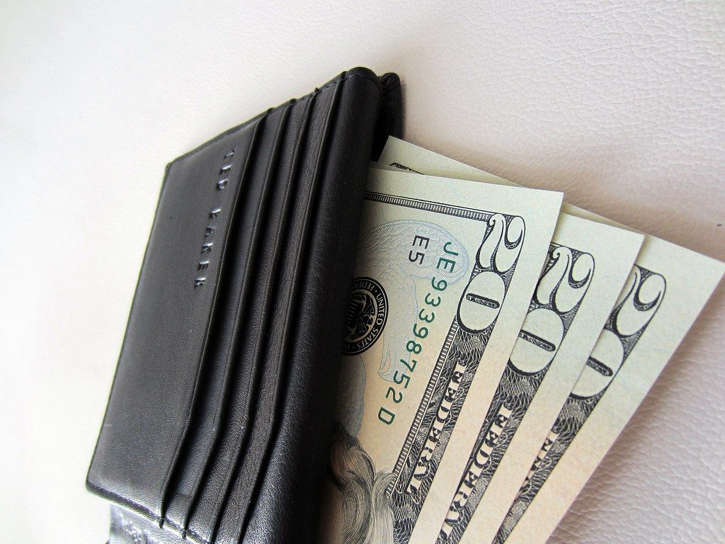 Black leather wallet with twenty dollar bills fanned out beside it