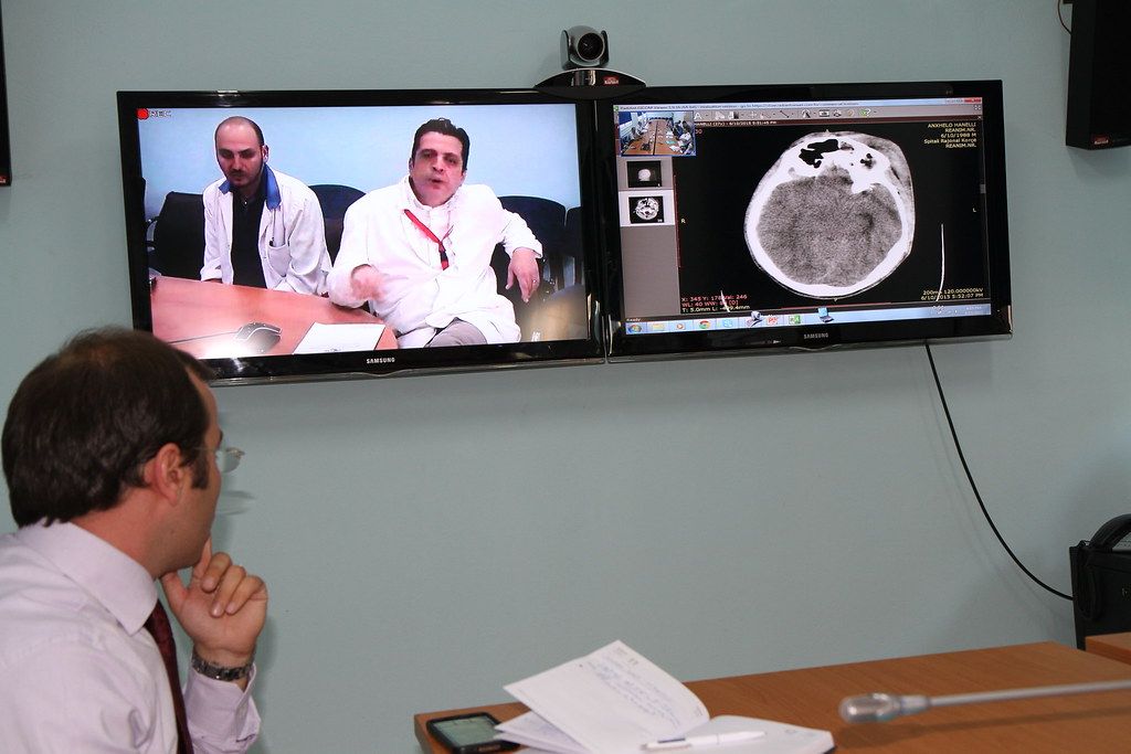 Clinician watching a video consultation on a wall-mounted screen with medical images