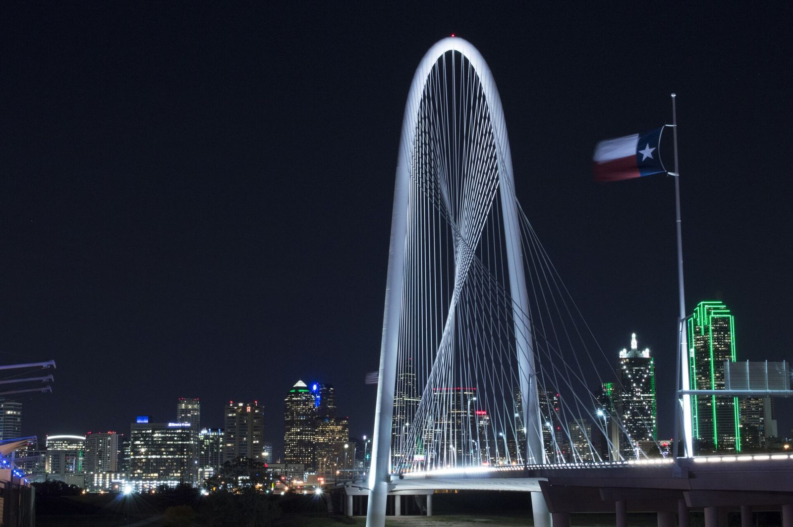 Margaret Hunt Hill Bridge lit at night with the Dallas skyline behind it