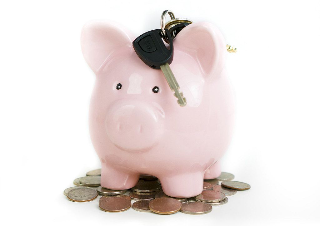 Pink piggy bank with a house key resting on top of a pile of coins