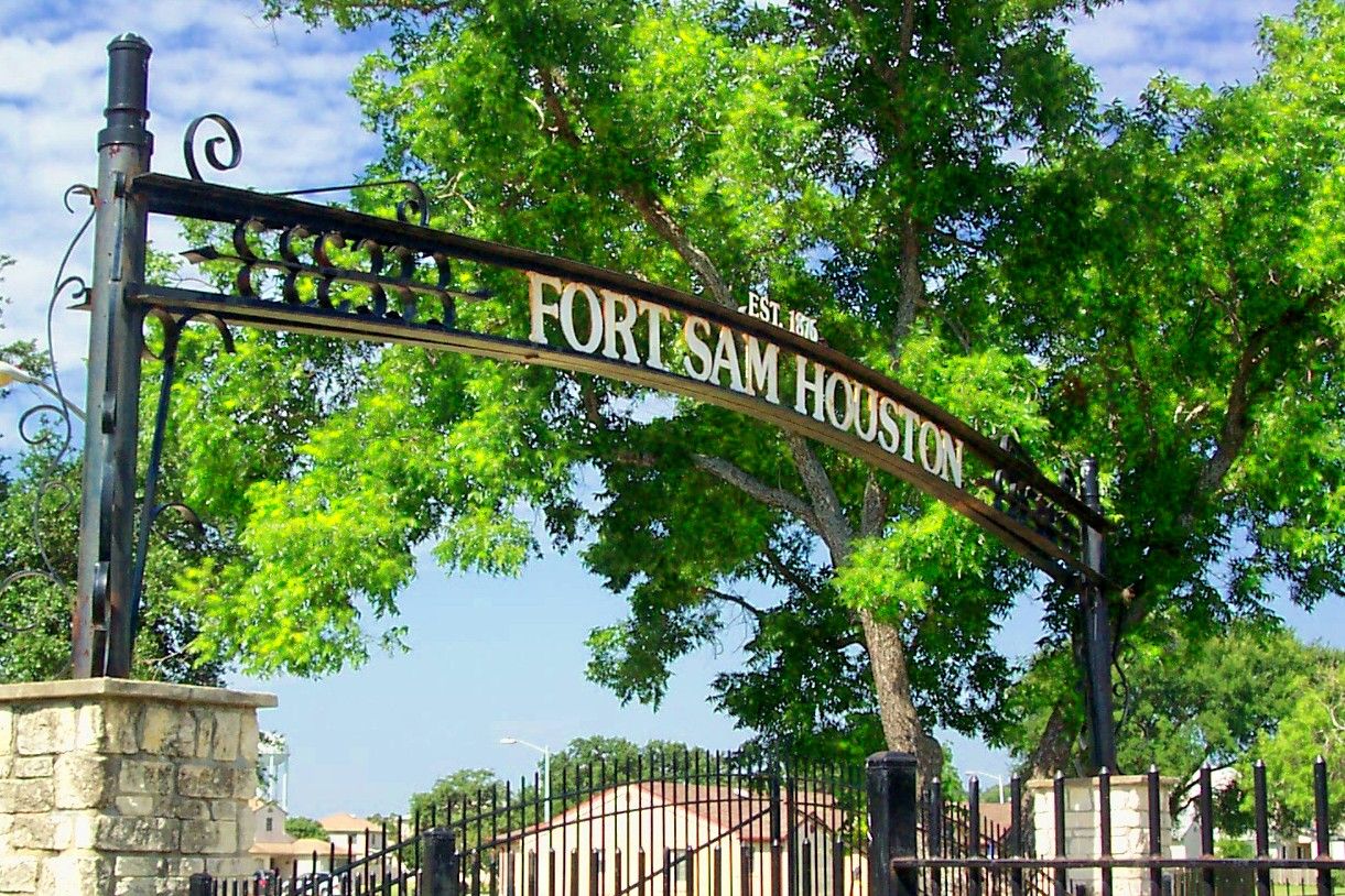 Arched iron entrance gate to Fort Sam Houston beneath shade trees