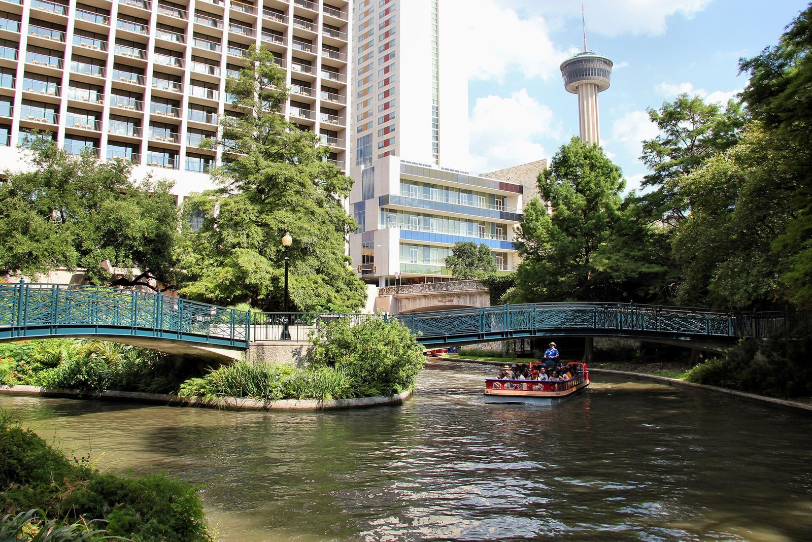 San Antonio River Walk with a footbridge, river barge and the Tower of the Americas