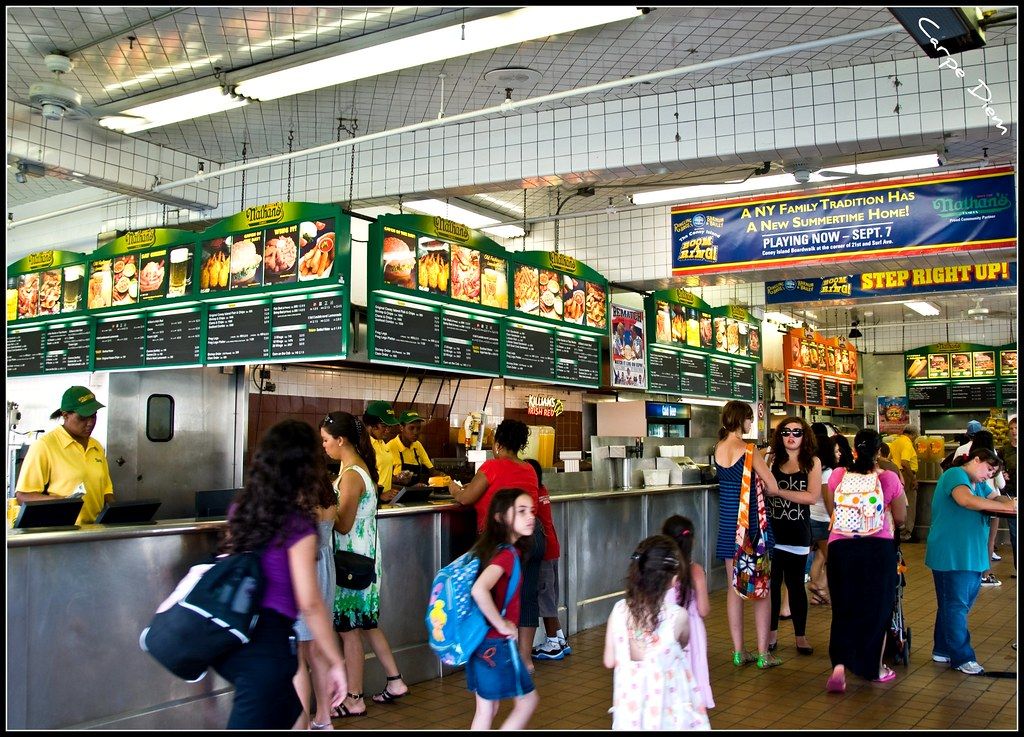 Busy fast-food counter with lit menu boards and customers waiting in line