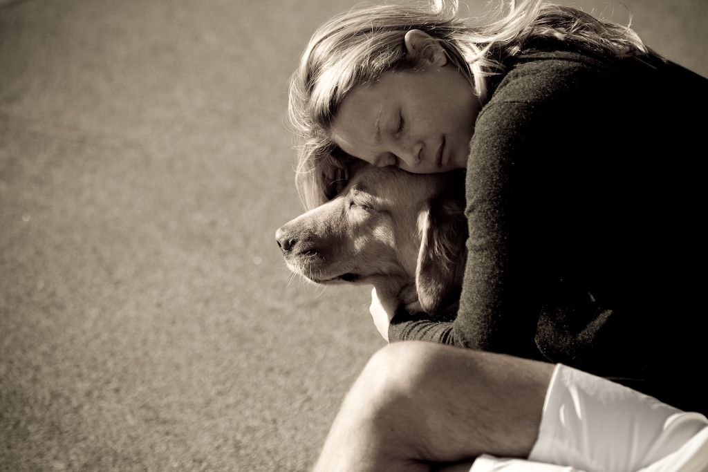 Woman with closed eyes hugging her dog close in a sepia-toned photo