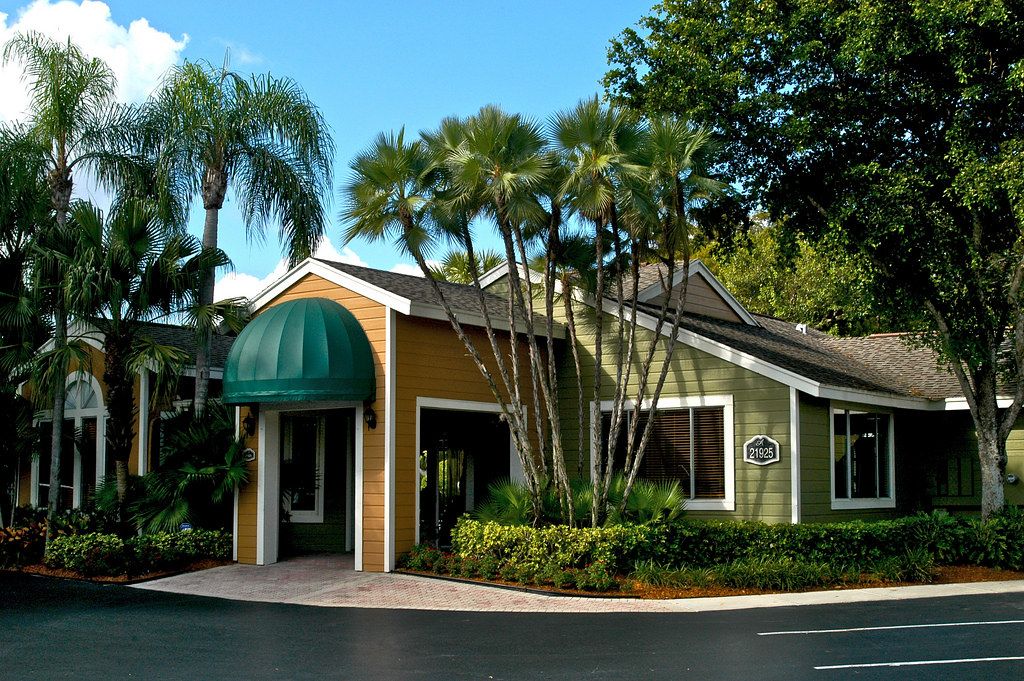 Apartment community leasing office with a green awning framed by tall palm trees