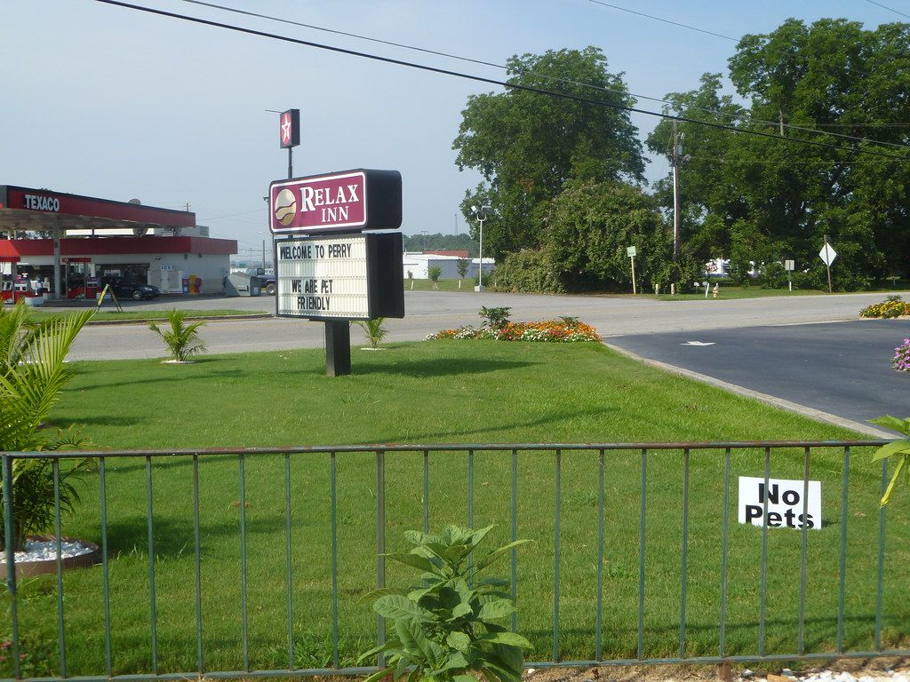Small no pets sign posted on a metal fence beside a motel sign and lawn