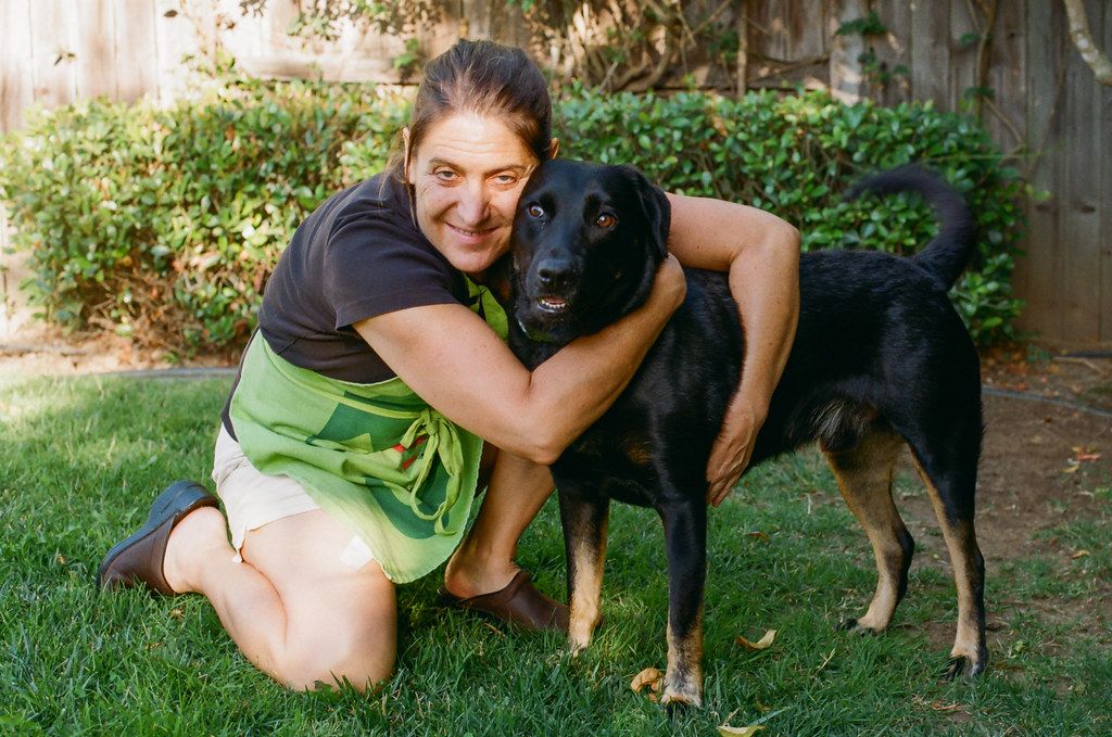 A woman kneeling in a garden with her arms around a dog