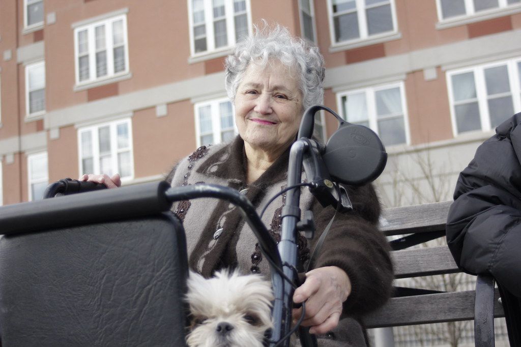 An older tenant outside an apartment building with a small dog